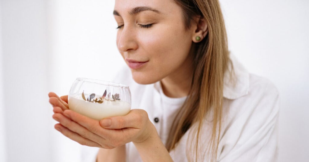 lady smelling candle in a glass bottle
